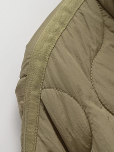 Detail shot of olive green quilted jacket featuring wave stitching and woven ribbon trim