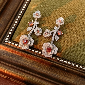 Detail of vintage flower earrings with red stones and white crystals on green fabric