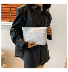 Detail of a white clutch bag with embossed bow texture held by a model in a leather shirt