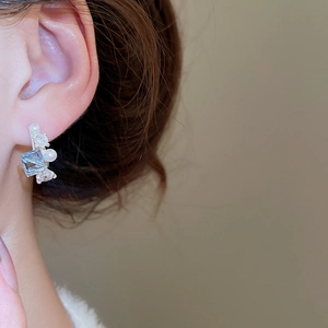 Close-up of pearl bow drop earrings featuring blue square zircon and silver finish