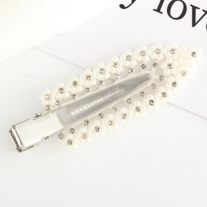 Close-up of a silver hair clip featuring white pearls and sparkling leaf-shaped rhinestones