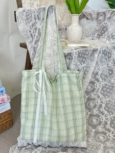 Green plaid tote bag with delicate white lace bow and ruffled trim on a wooden chair