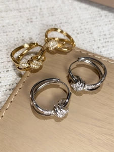 Detailed view of gold and silver knot earrings with pavé crystals on a soft leather mat