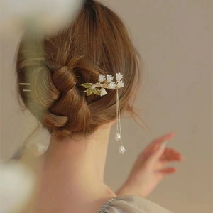 Épingle à cheveux muguet élégante avec pompon doré et perles sur un chignon soigné