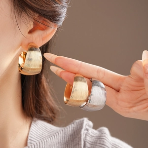 Detailed close-up of textured C-shaped hoop earrings in gold and silver finishes