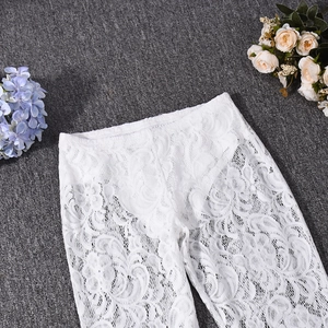 Close-up of white lace pants with intricate floral embroidery on textured grey fabric