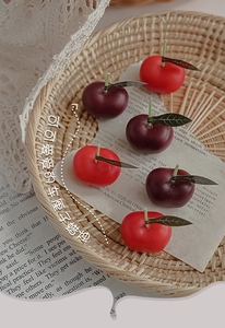 Detalle de velas con forma de cereza roja y tallos verdes en una cesta rústica