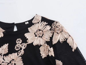 Detail van zwarte mesh jurk met beige bloemenborduursels en maatlabel S in de nek