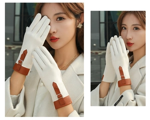 Detail of cream suede gloves featuring brown leather buckle straps and hand-made label