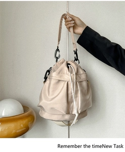 Detail of beige nylon bucket bag featuring a drawstring closure and black metal hooks