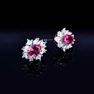 Macro shot of oval red ruby-style earrings with white zircon halo on black reflective surface