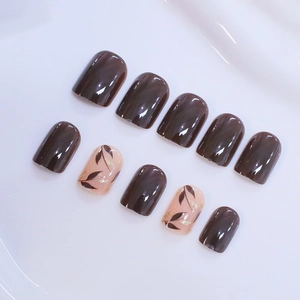 Short square press-on nails in deep brown with gold glitter leaf designs on a white background