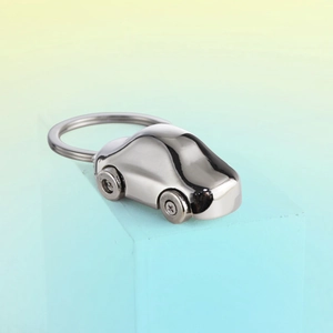 Polished silver metal car-shaped keychain on a modern light blue geometric pedestal