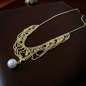 Detail of gold lace-texture beaded necklace featuring a large white pearl pendant