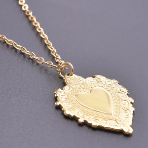 Macro shot of gold sacred heart pendant with intricate vintage patterns and fine O-chain
