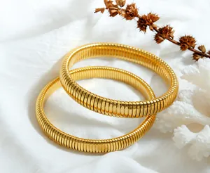 Detail showing two gold Tubogas stretch bracelets with spiral metallic texture on white fabric