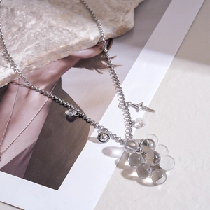 Macro detail of silver necklace with glass grape clusters and star charms on stone surface