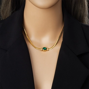 Close-up of golden snake chain necklace featuring a round green gemstone on a model