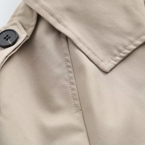Détail des coutures d'un trench-coat kaki et d'un bouton noir mat sur le revers