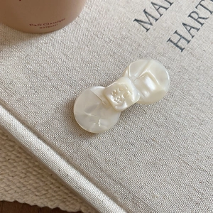 Detailed close-up of cream resin hair clip featuring engraved text and pearlescent finish