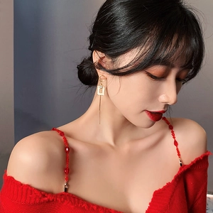 Close-up of golden asymmetric long earrings styled with a red off-shoulder knit top
