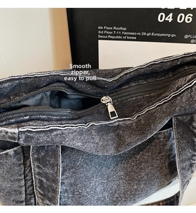 Detail shot of the durable metal zipper and white stitching on a gray denim tote bag