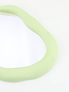 Detail of light green irregular wavy frame on a minimalist matte finish vanity mirror