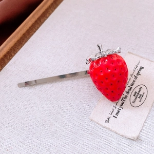 Macro shot of a red strawberry hair clip with silver metal barrette on beige linen fabric
