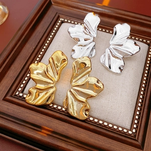 Macro detail of leaf-textured gold and silver earrings on a vintage pearl-rimmed tray