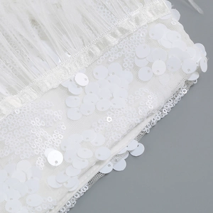 Detailed macro view of white ostrich feathers and sparkling sequins on mesh fabric