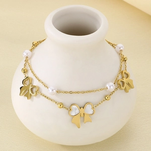 Detail of 18K gold-plated double-layer bracelet with bow charms and pearls on a white vase