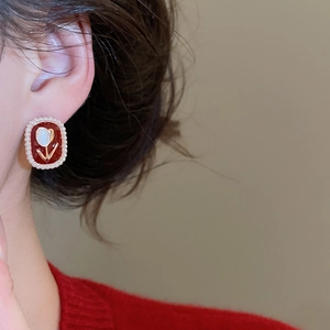 Close-up of red tulip enamel earrings with pearl border on model wearing red sweater