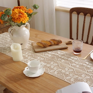 Detailed view of beige crochet lace table runner with hollow floral pattern and tassels