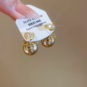 Macro detail of heart-shaped gold earrings with white zircon and champagne pearls