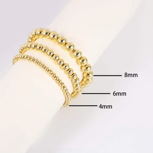 Dettaglio di bracciali con perle dorate da 4mm, 6mm e 8mm su pilastri bianchi