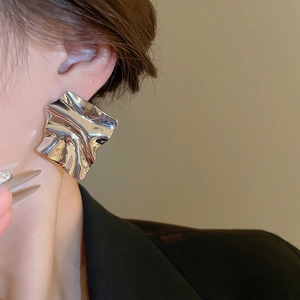 Close-up of large silver irregular pleated metal earrings on a model's ear