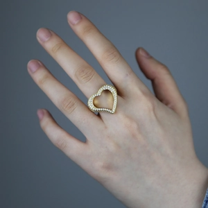 Detail of a hollow heart-shaped gold ring with zircon pavé setting on a model finger