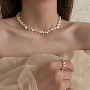 Detail shot of irregular baroque pearl necklace and gold chain ring on a female model