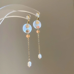 Detail of elegant gold drop earrings with circular shells, chains and white pearls