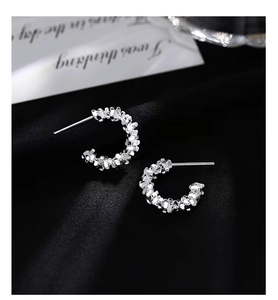Macro shot of silver C-shaped earrings with irregular crushed silver texture on dark velvet