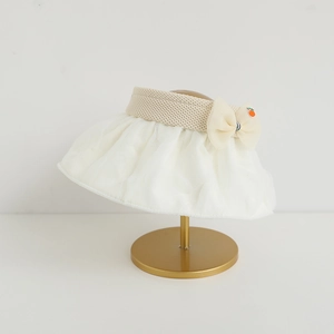 Detail of girls beige sun hat with mesh brim, bow tie and orange charm on gold stand
