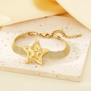 Golden woven mesh strap bracelet with star pendant on a textured stone display