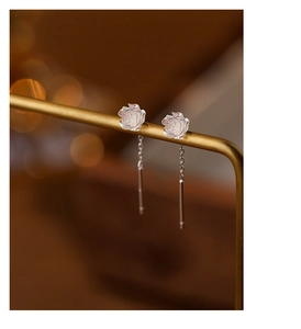 Macro shot of iridescent white rose earrings with silver tassels on a gold stand