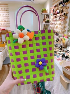 Detail of green and purple checkered woven handbag with plush flower and heart charms