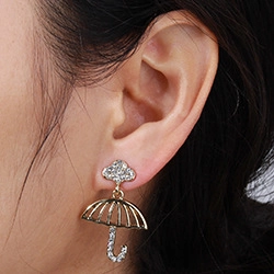 Detailed view of a model wearing gold cloud and umbrella earrings with white rhinestones