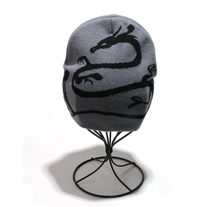 Detail of grey knitted beanie featuring a black dragon pattern on a metal stand