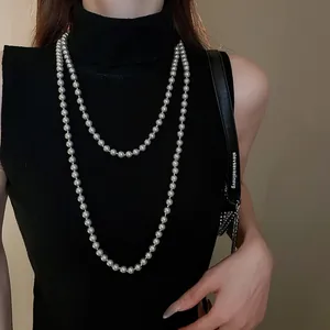 Elegant long silver-grey faux pearl necklace worn in double layers over a black sweater