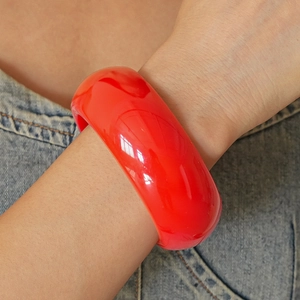 Detail of a bold red resin geometric bangle worn over denim for a modern stylish look
