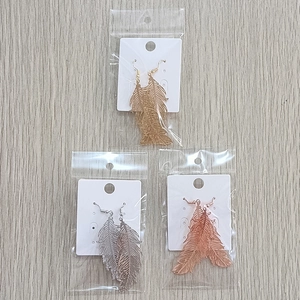 Detail of feather-shaped earrings in gold, silver, and rose gold with hollow metal textures