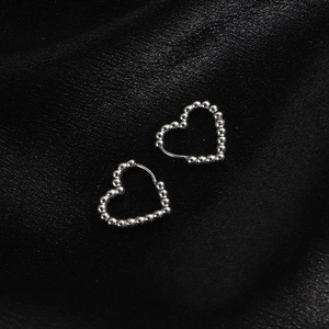 Detail von silbernen herzförmigen Perlenohrringen auf elegantem schwarzem Seidenhintergrund